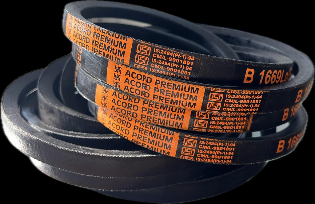 A close-up image of several black industrial V-belts stacked on a light colored wooden table. Text on the belts is blurry and unreadable